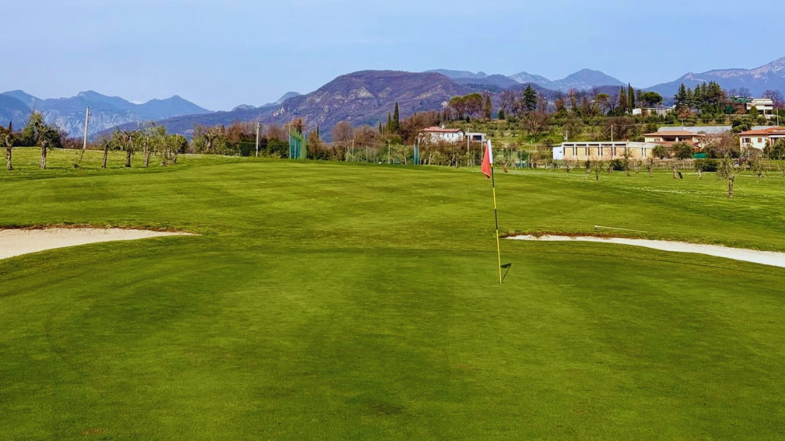 Wide view of a lush green golf course fairway and putting green with mountains in the background during a sunny day.