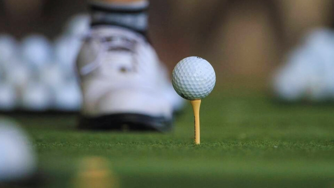 Close-up of a white golf ball on a yellow tee with a golfer's white shoe blurred in the background