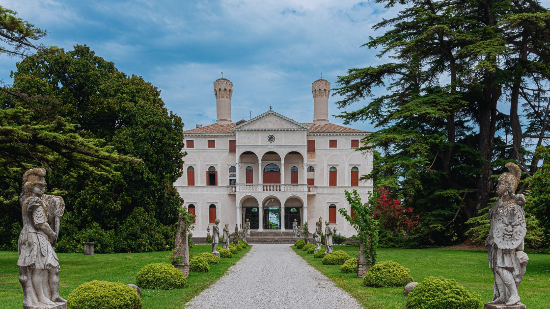 Symmetrical view of the Renaissance villa at Castello di Roncade, featuring a pebble path lined with stone statues and lush green gardens in Treviso, Italy