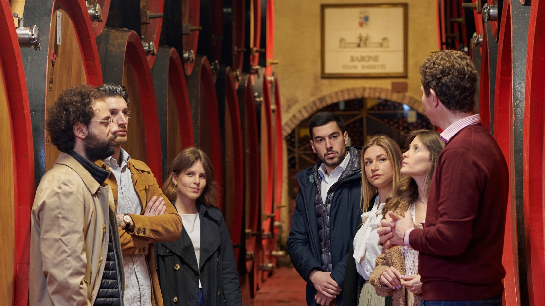 Group of people during a guided wine tour at Castello di Roncade winery, surrounded by large red oak barrels.