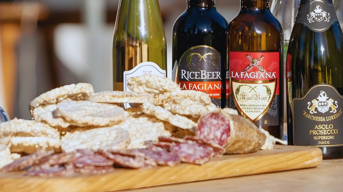 A gourmet selection of Azienda Agricola La Fagiana products, featuring artisanal rice beer, Asolo Prosecco, and local cured meats served with crispy rice cakes.